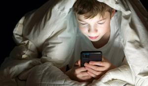 Primary school boy under the covers reading on his smart phone.