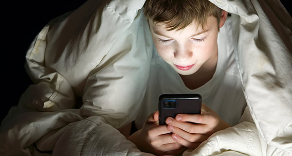 Primary school boy under the covers reading on his smart phone.