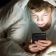 Primary school boy under the covers reading on his smart phone.